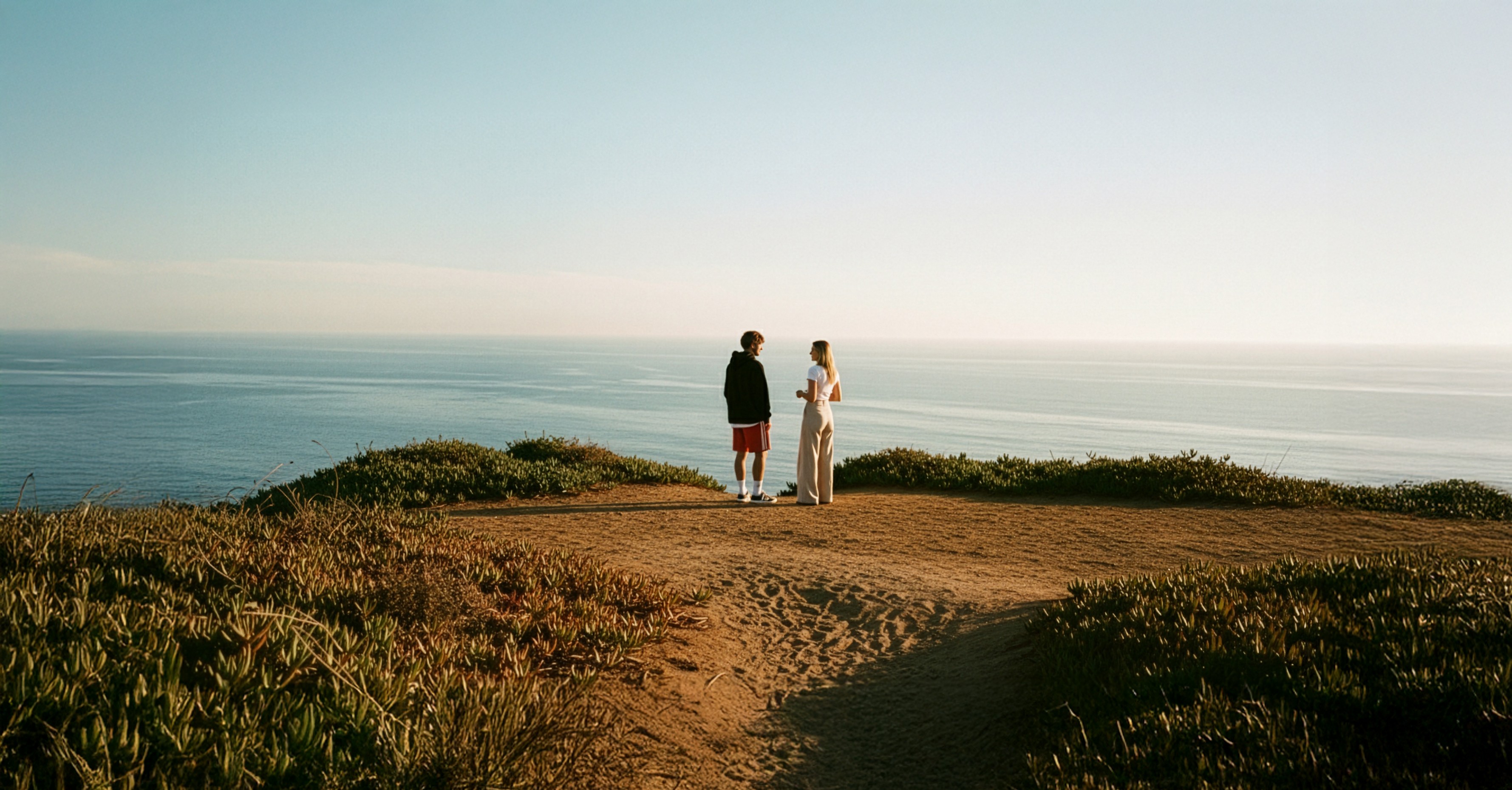 omage of two people standing on a cliff, talking and overlooking the wide ocean